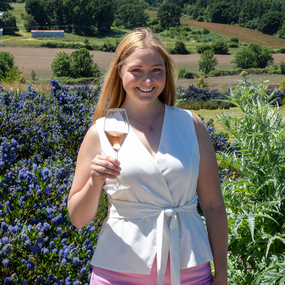 Haley Vachter holding glass of Brut Rosé in front of purple flower bed